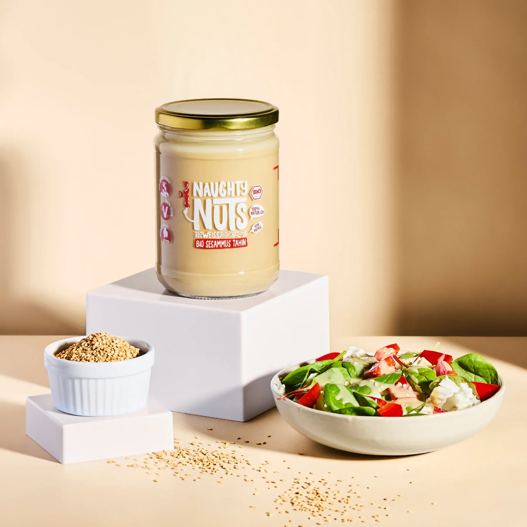 Bio Sesammus Tahin weiß im Glas auf einem Podest neben einer Schale mit Salat und Sesamsamen