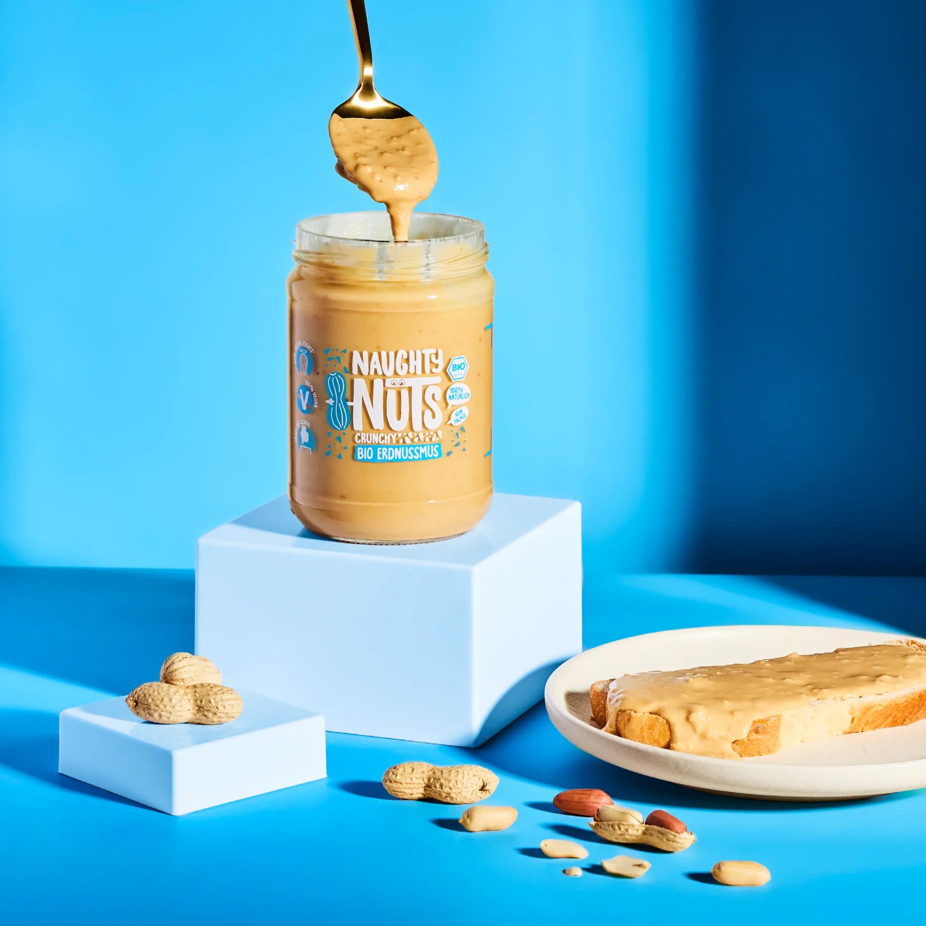 Bio Erdnussmus Crunchy im Glas mit Löffel auf blauem Hintergrund
