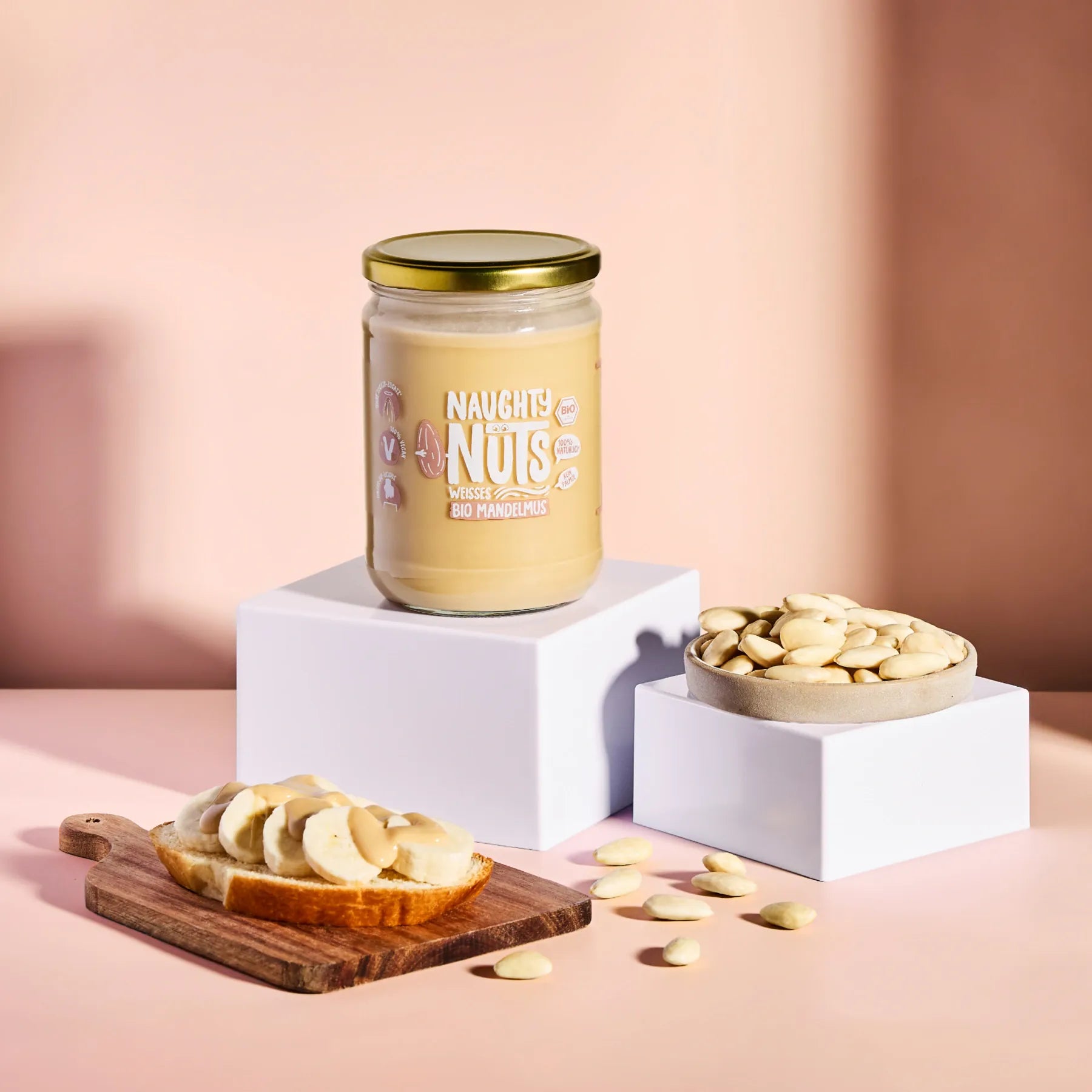 Bio Weisses Mandelmus im Glas auf einem Podest mit Bananenbrot und Mandeln