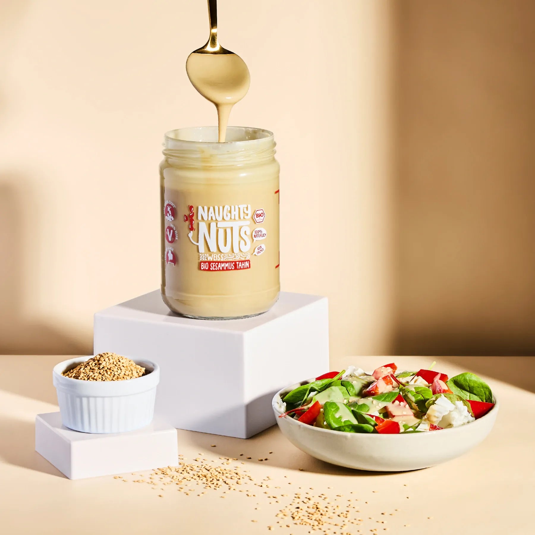 Bio Sesammus Tahin weiß im Glas mit Löffel über einer Schale mit Salat und Sesamsamen