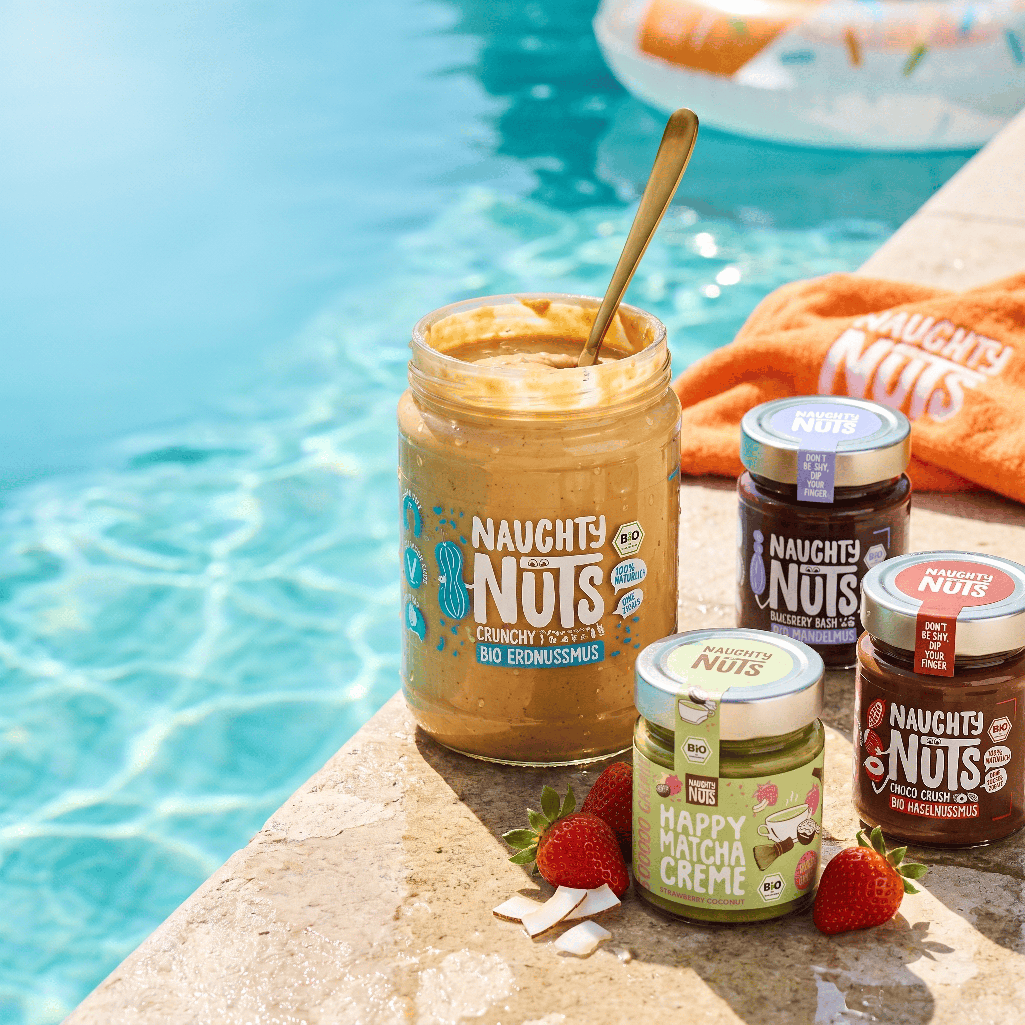 Naughty Nuts Produkte am Poolrand mit Erdbeeren und Kokosnussstücken